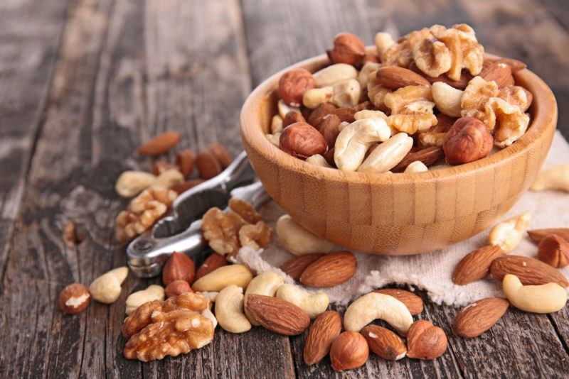 A wooden bowl of nuts, with more nuts on a table