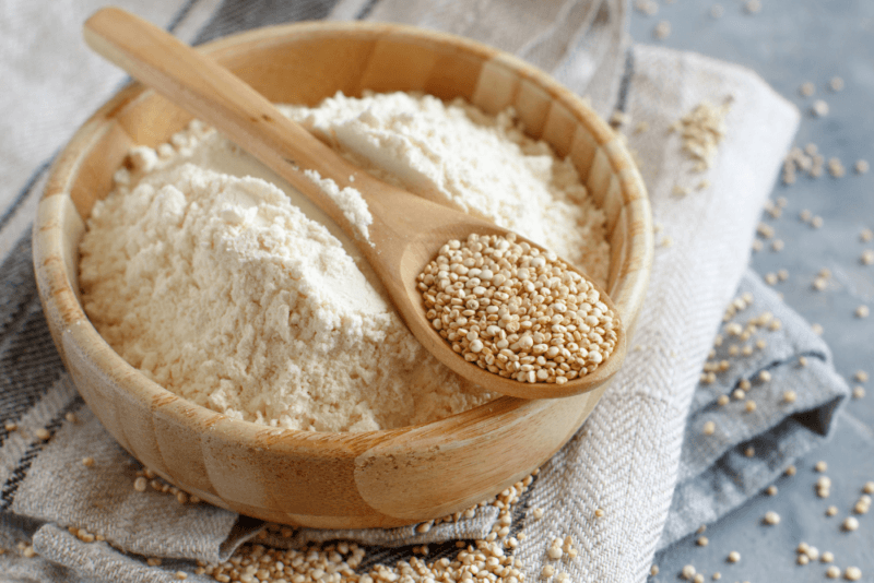 A cloth with a large bowl of quinoa flour and a wooden spoon containing quinoa seeds