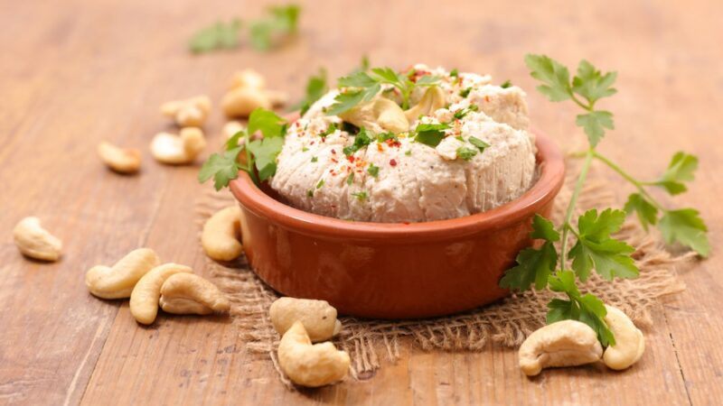 A red bowl filled with vegan cashew cheese, surrounded by cashews