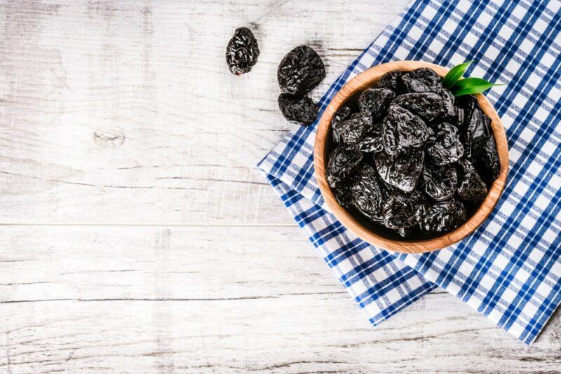 A small brown bowl of prunes on top of a blue and white cloth