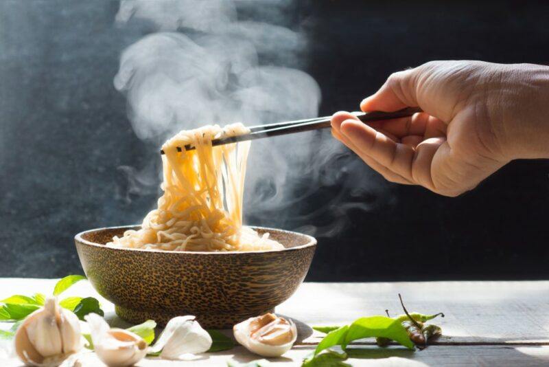 A steaming bowl with noodles that someone is using chopsticks on