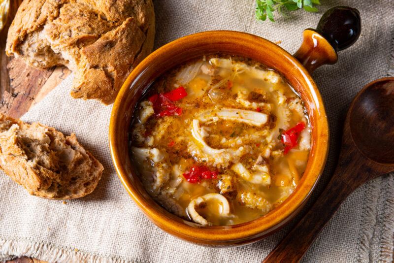 A brown bowl of tripe soup next to brown bread