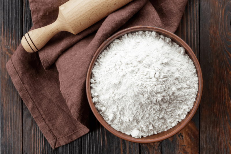 A wooden table with a cloth, a rolling pin, and a bowl of flour