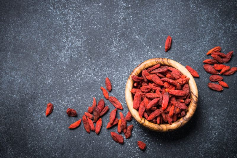 A top down image of a brown bowl of goji berries on a black background