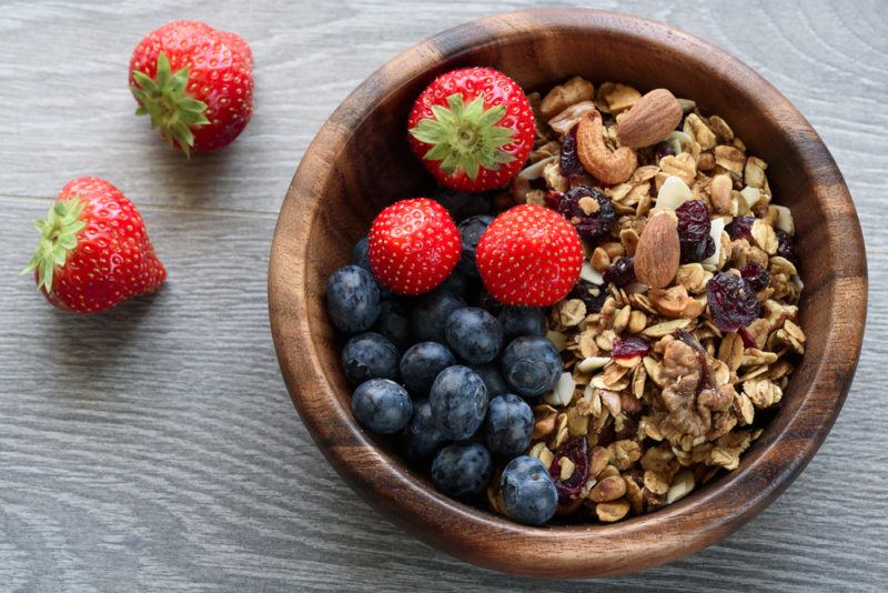 A wooden bowl that contains granola that has been topped with strawberries and blueberries