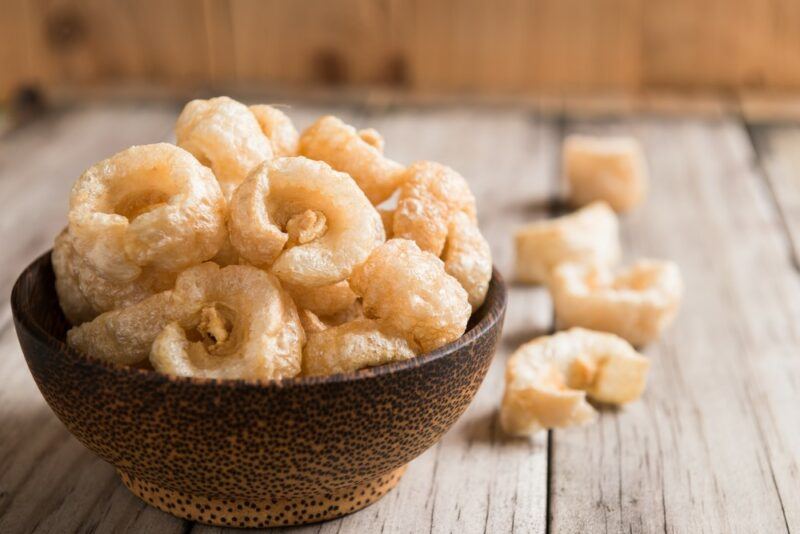 A brown bowl filled with dried pork rinds, with a few more scattered on the table