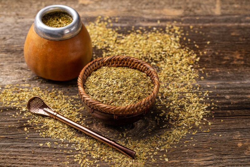 A small wooden bowl of yerba mate with a spoon, next to a gourd of the tea