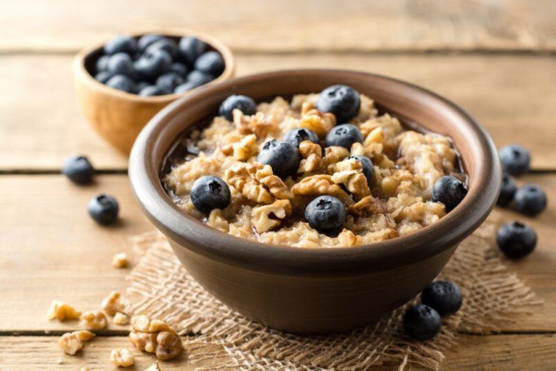 A small brown bowl with oatmeal that's topped with nuts and blueberries, next to a small bowl of blueberries