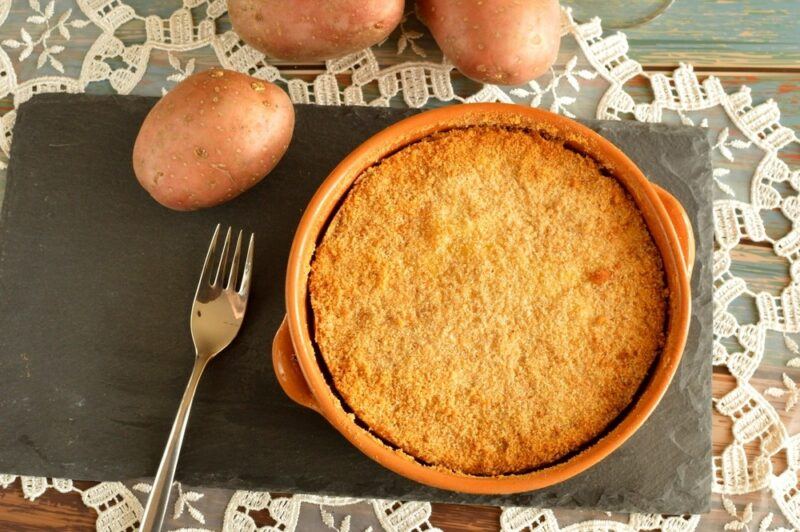 A dish containing sweet potato pudding, next to a fork and some sweet potatoes