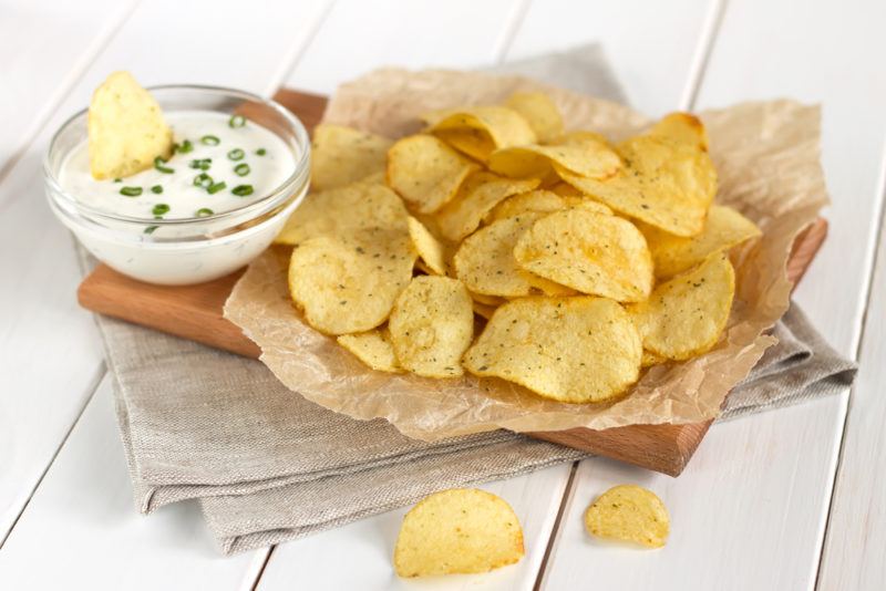 A brown piece of paper with chips and dip | Food For Net A wooden board with paper, with fried chips and white dip
