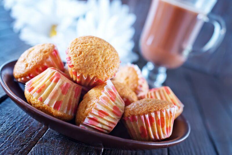 A brown plate containing small muffins with hot chocolate in the background