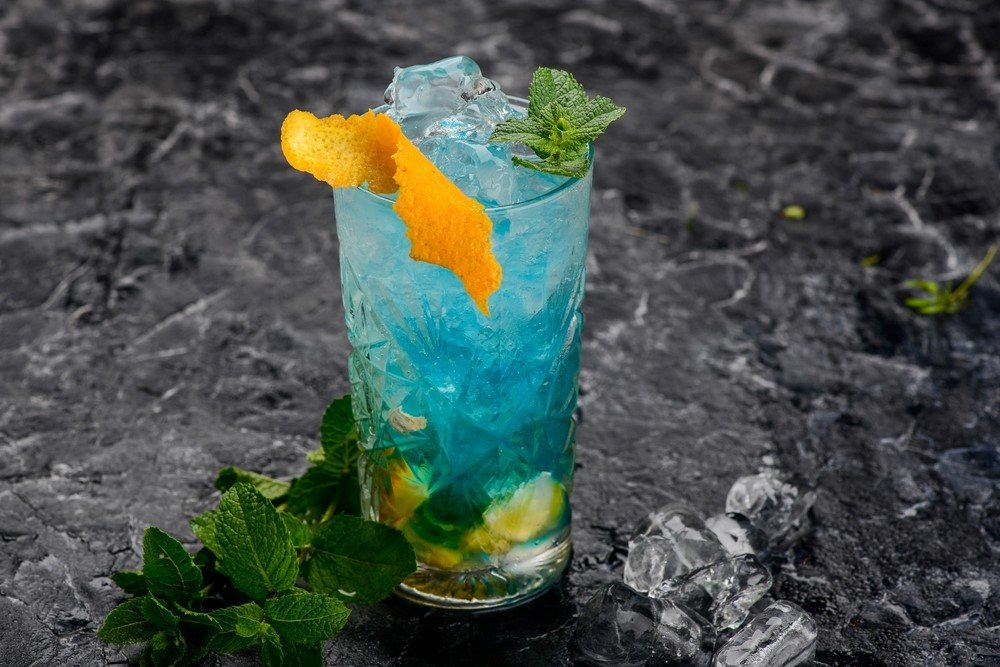 A gray table with a glass of a bullfrog cocktail with ice, garnished with an orange twist