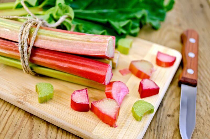 A wooden tray with a bunch of rhubarb, where some pieces have been cut, next to a knife