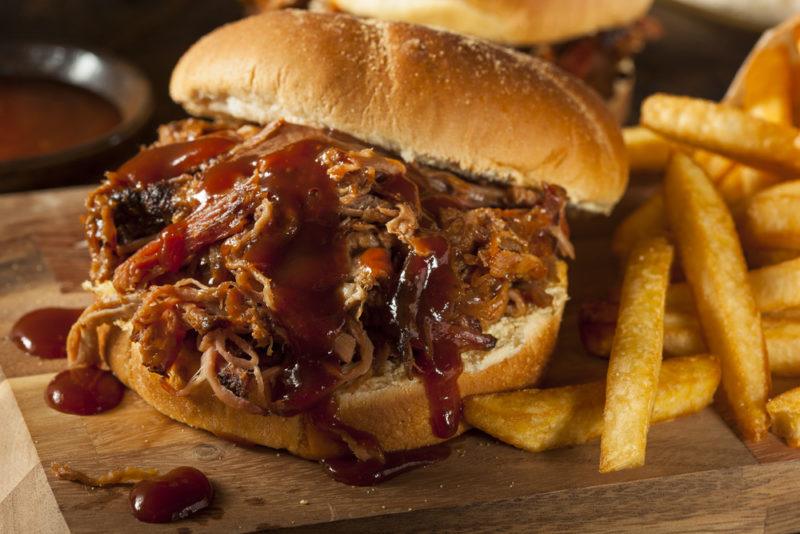 A wooden board with a pulled pork burger and fries