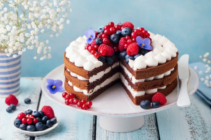 A white cake stand with a layered cake topped with berries