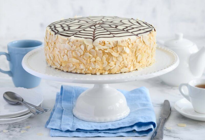 A cake stand with an almond and white chocolate cake with chocolate webs on the top