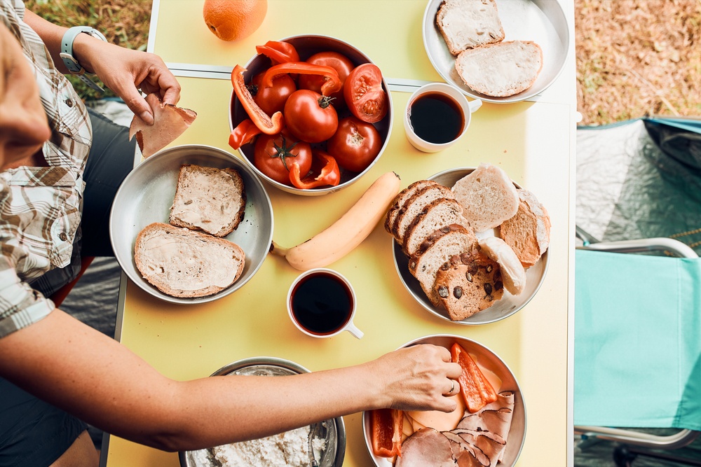 A camping table with a selection of food, including bread, red peppers, meat, and more