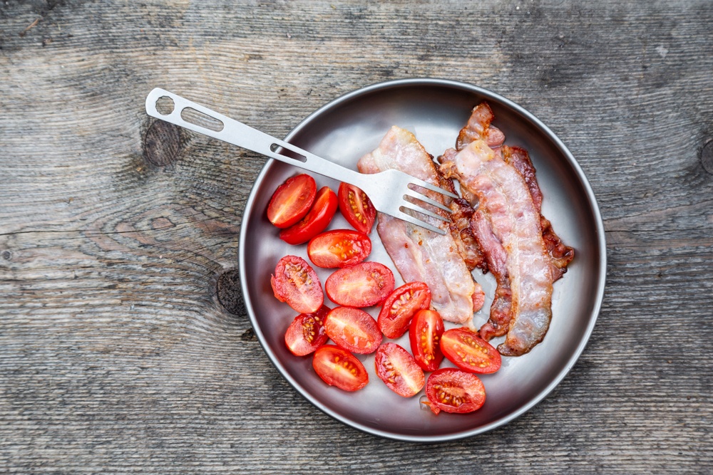 A frypan with cooked tomatoes and bacon, with a fork