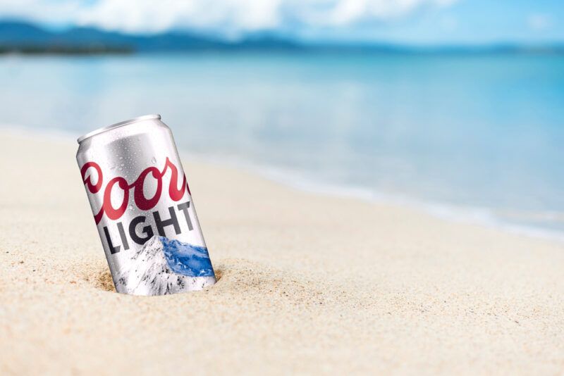 A can of Coors light beer on the beach with almost white sand and light blue water