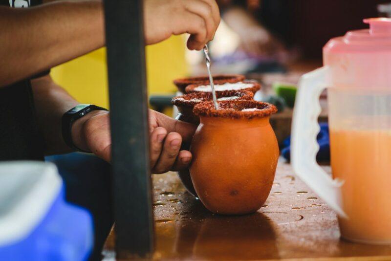 Two mugs of a cantarito cocktail being made by a street vendor