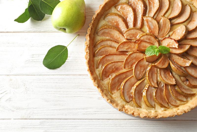 A dish of pear and caramel pie on a white deck or table with an apple or pear next to it