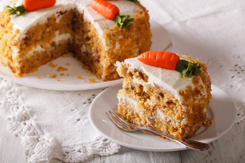 A carrot cake with icing carrots on the top and a piece cut out of it