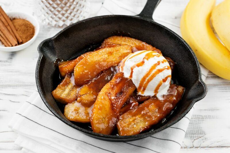 A cast iron fry pan containing bananas foster, plus a scoop of ice cream drizzled with sauce