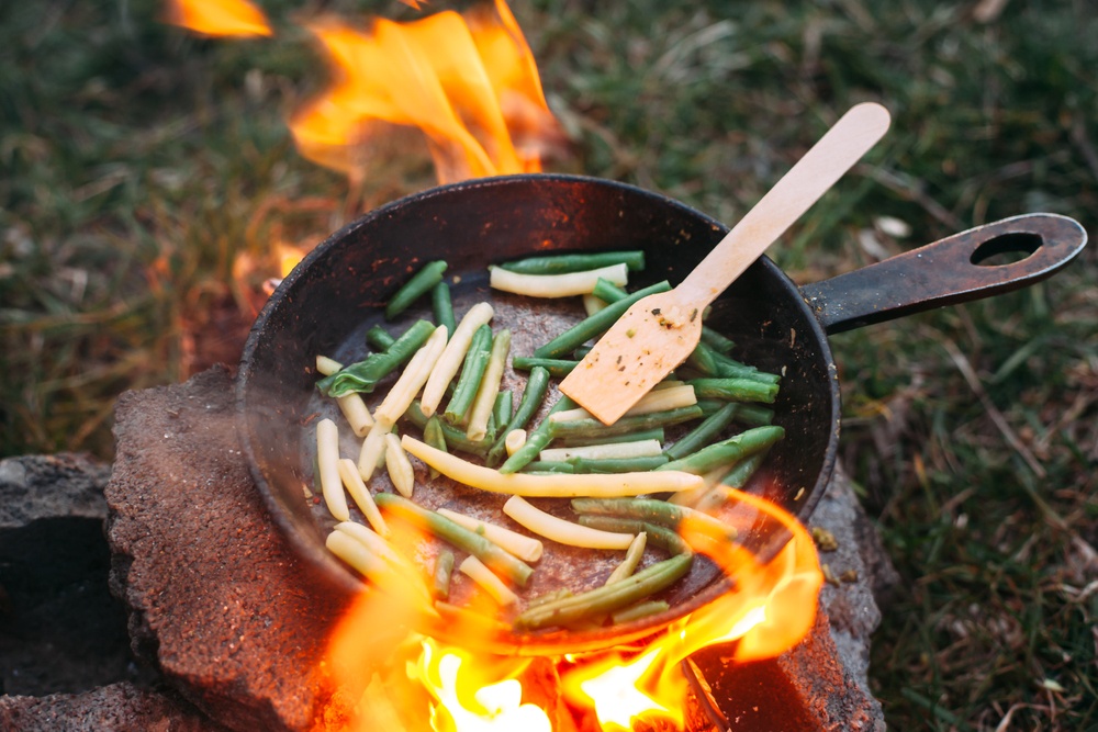 A frypan on a camp fire with white and green beans