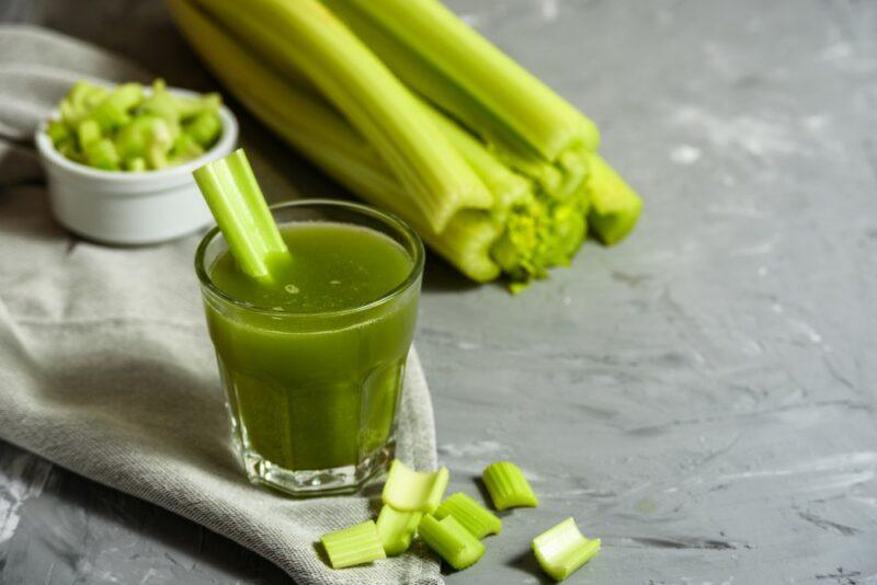 A glass of celery juice next to sticks of celery and some chopped celery