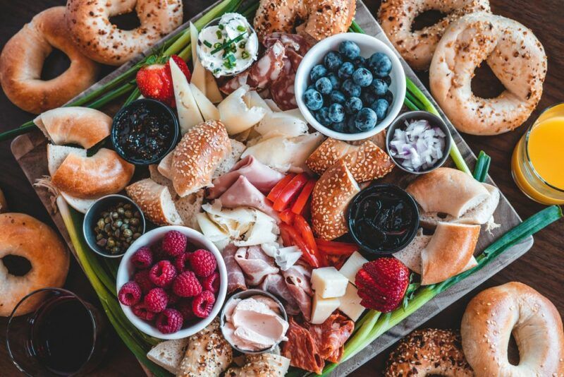 A picnic charcuterie board containing fresh fruit, bagels, spreads, meat, and more