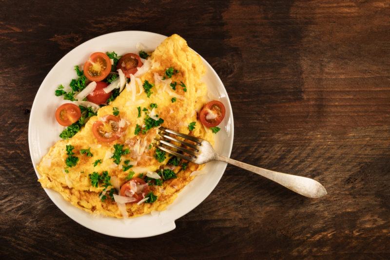 A white plate that holds a cheesy omelet with tomato and greens