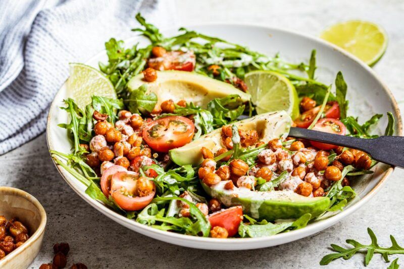 A large plate that contains a chickpea salad with avocados, tomatoes, and lime