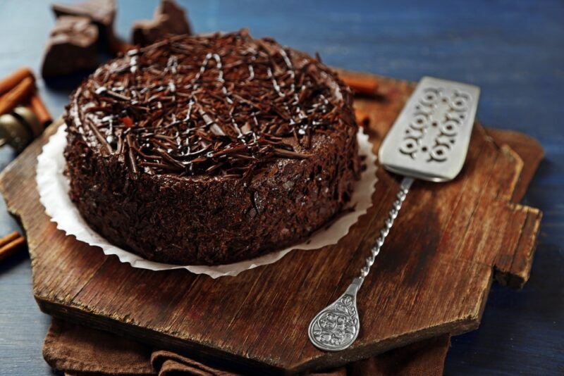 A wooden tray with a chocolate Chinese five spice cake, next to a metal spatula