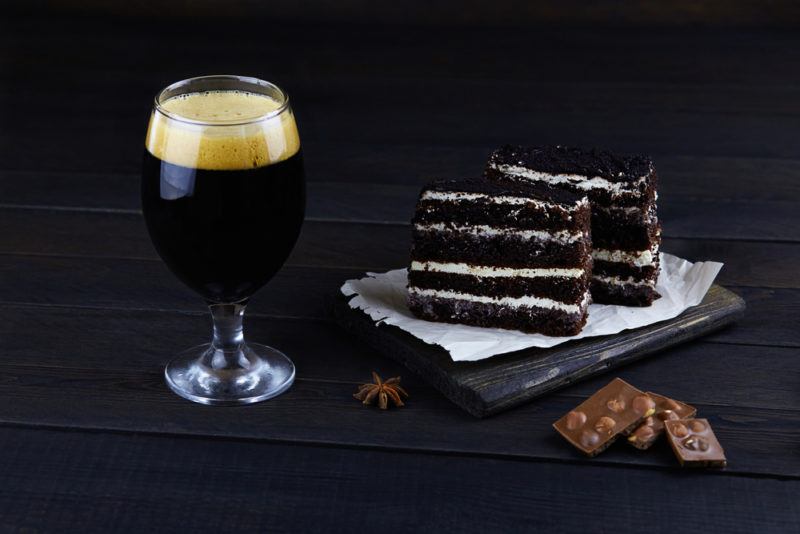 A dark chocolate cake next to chocolate stout on a wooden table