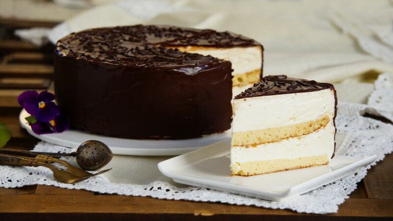 A Russian cake called ptichye moloko or birds milk, with chocolate icing and a piece cut out of it