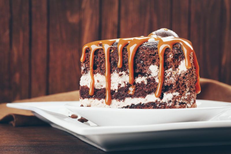 A single piece of cake on a white plate covered in caramel sauce