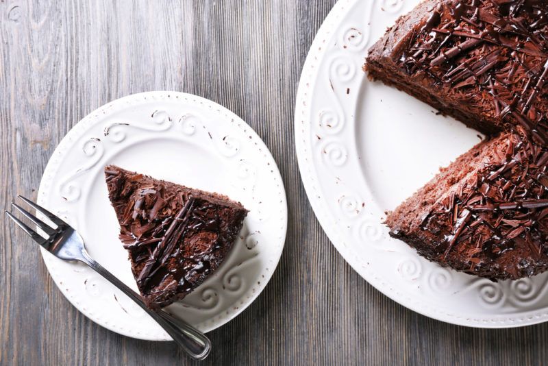 A large white plate of chocolate cake with a piece cut out of it