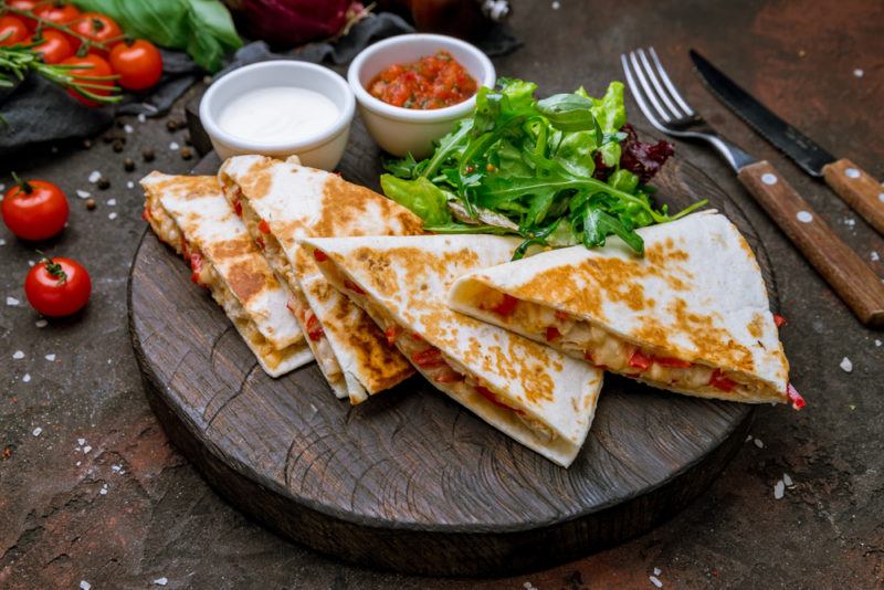 A wooden dish with quesadillas with dipping sauce and greens