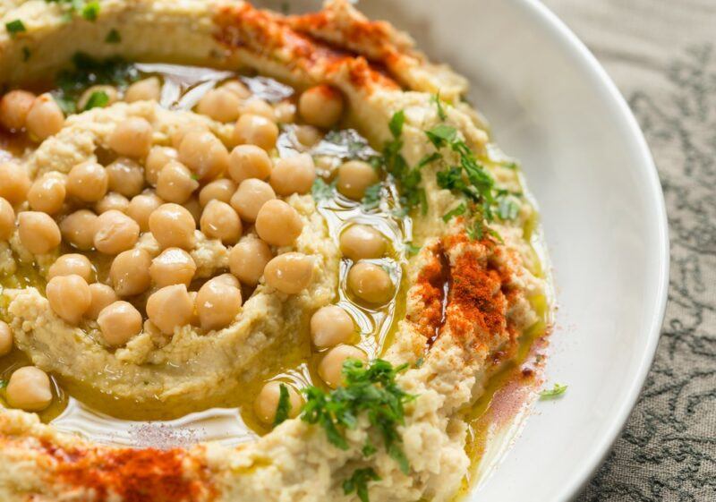 A large white bowl containing hummus and fresh chickpeas