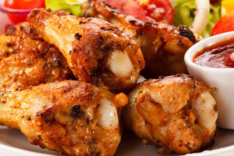 A close up image of chicken drumsticks for dinner next to some dipping sauce