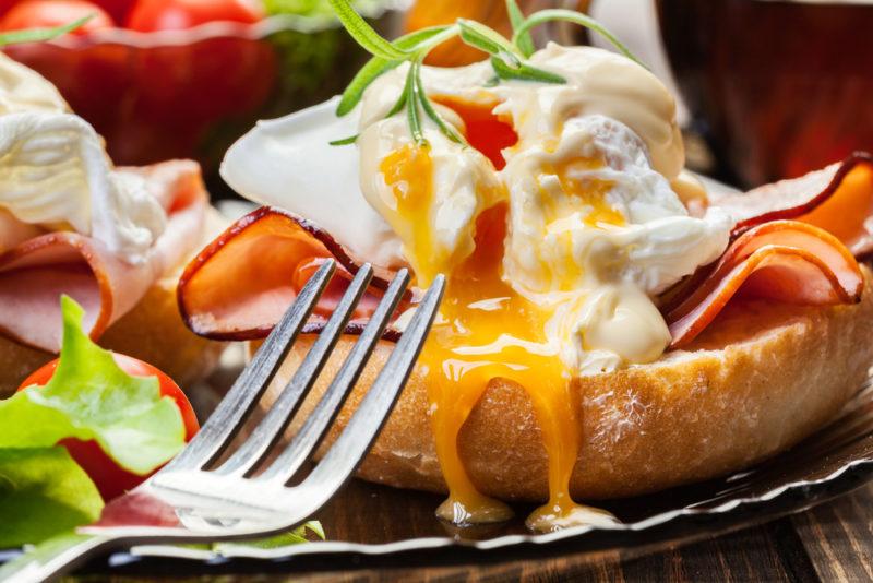 Eggs benedict served on a plate with a fork. The egg has been broken and is running down the bread