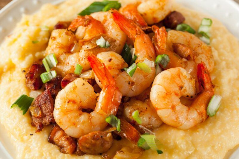 A close up image of grits with cooked shrimp and some greens on top