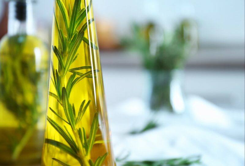 A close up image of two bottles of rosemary olive oil, with a blurry bottle of herbs in the background