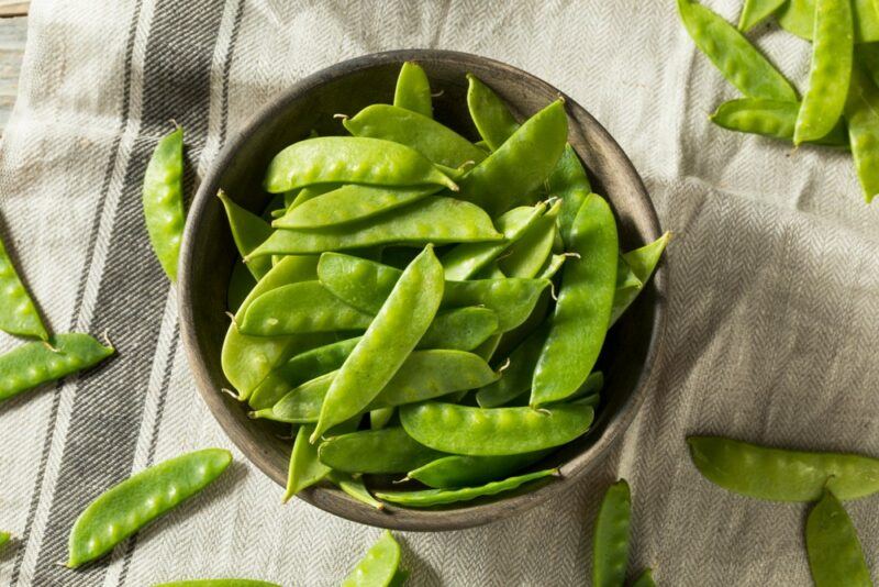 A cloth with a selection of snow peas, plus a bowl that contains a large number of the peas