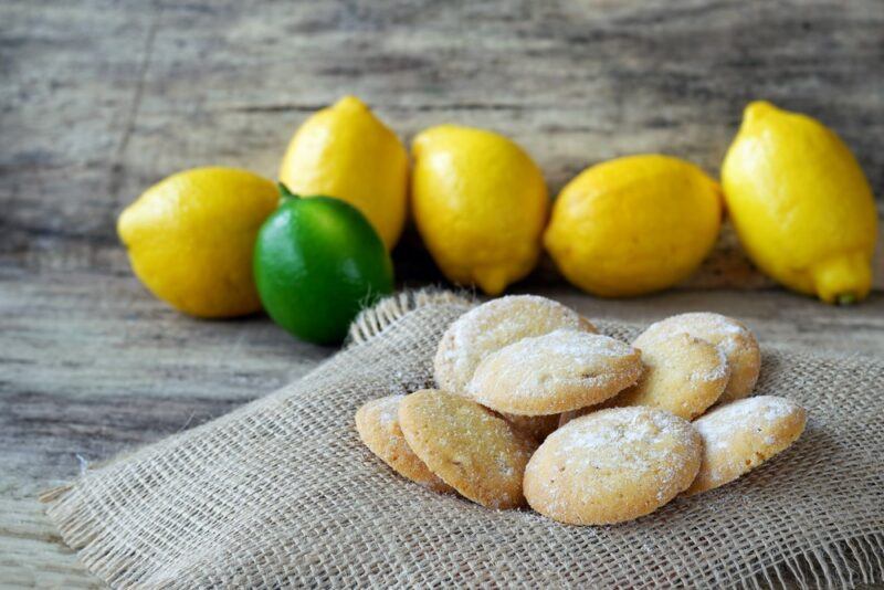 A piece of cloth with lemon olive oil cookies in front of a selection of lemons and one lime