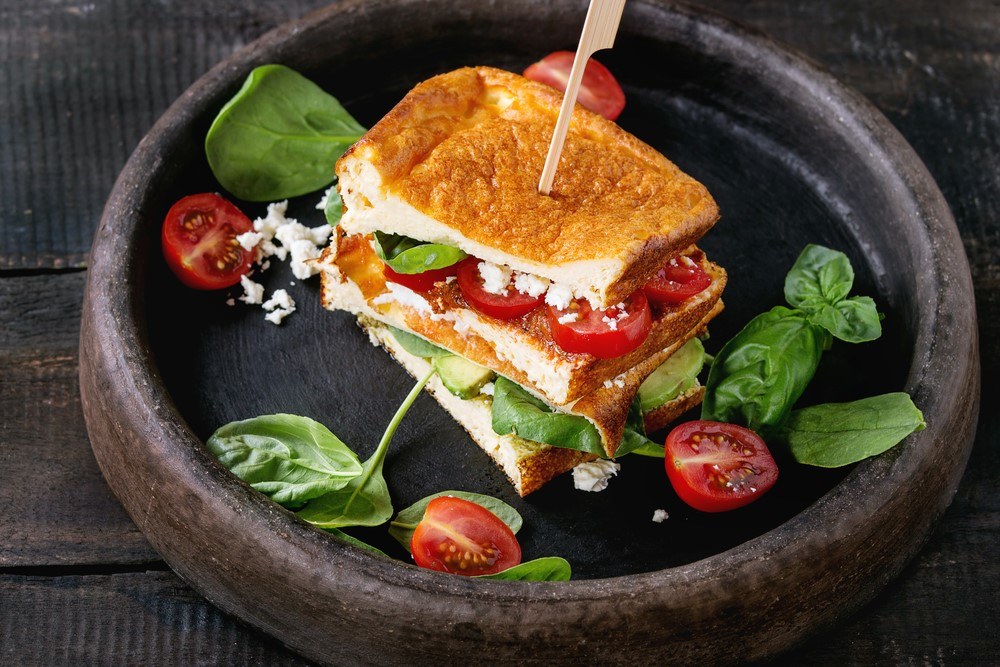 A dish that contains a sandwich made from cloud bread, along with spinach and tomatoes