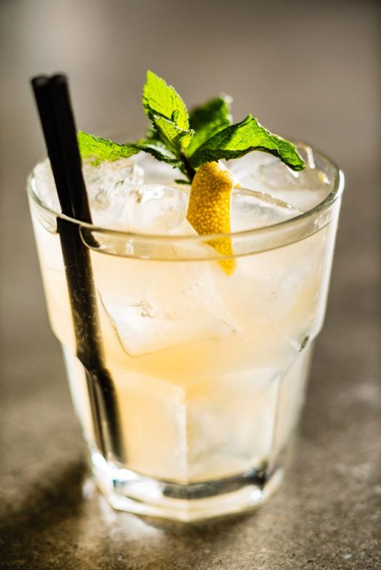 A cocktail called The Bone in a short glass with ice and two cocktail straws 