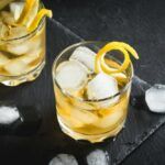 A black table with pieces of ice and two cocktails called an evening in Mexico