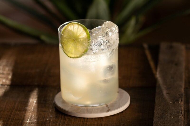 A glass containing a cocktail called evening in Mexico, with plenty of ice and a slice of lime