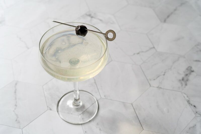 A white table with an original sin cocktail that's been garnished with a single olive